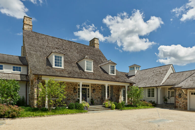 Entry court of cottage-style Chestnut Fields, a Chester County farmhouse with stone and siding exterior walls, front porch, sweeping cedar shake roof, dormers and cupola.