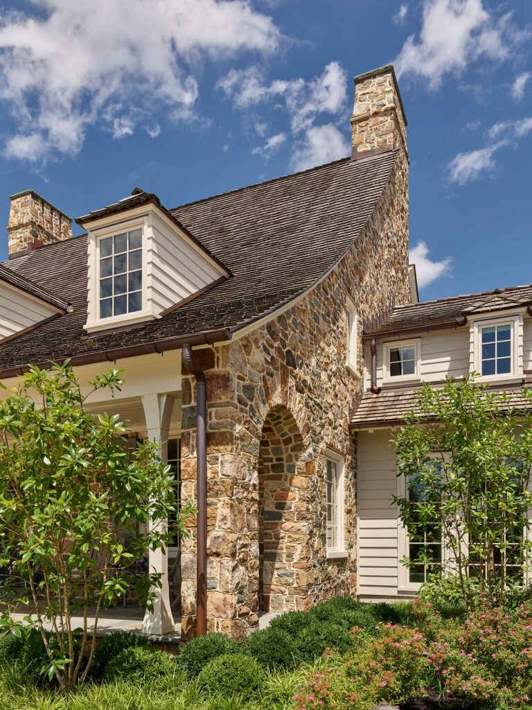 Detail of cottage-style entry to Chestnut Fields, a Chester County farmhouse with stone arched opening, dormers and sweeping cedar shake roof.