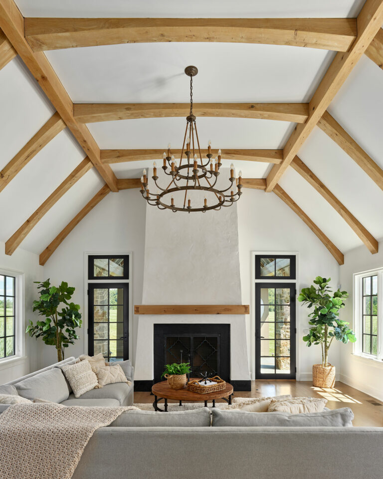 Family room in Chestnut Fields, a contemporary farmhouse in Chester County with white walls, black frame doors and windows, timber frame vaulted ceiling, and fireplace with wood mantel.