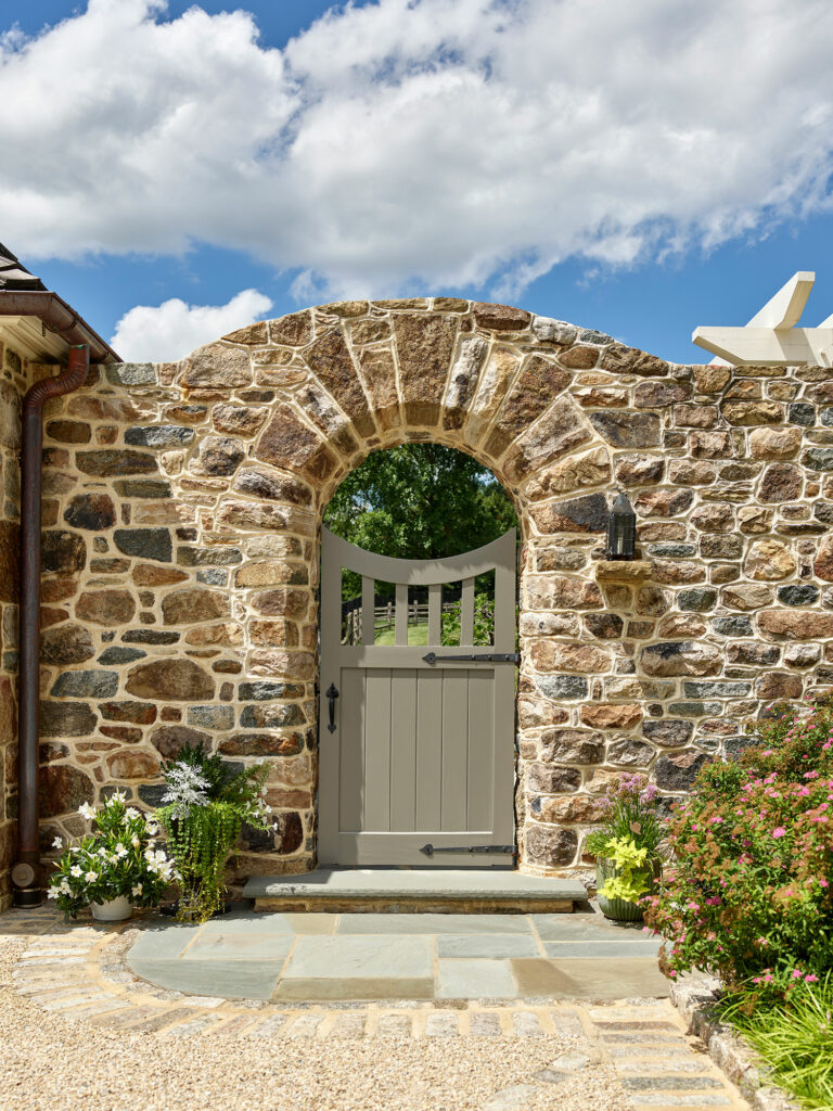Arched stone opening with custom gate leading from entry court of Chestnut Fields, a Chester County farmhouse.
