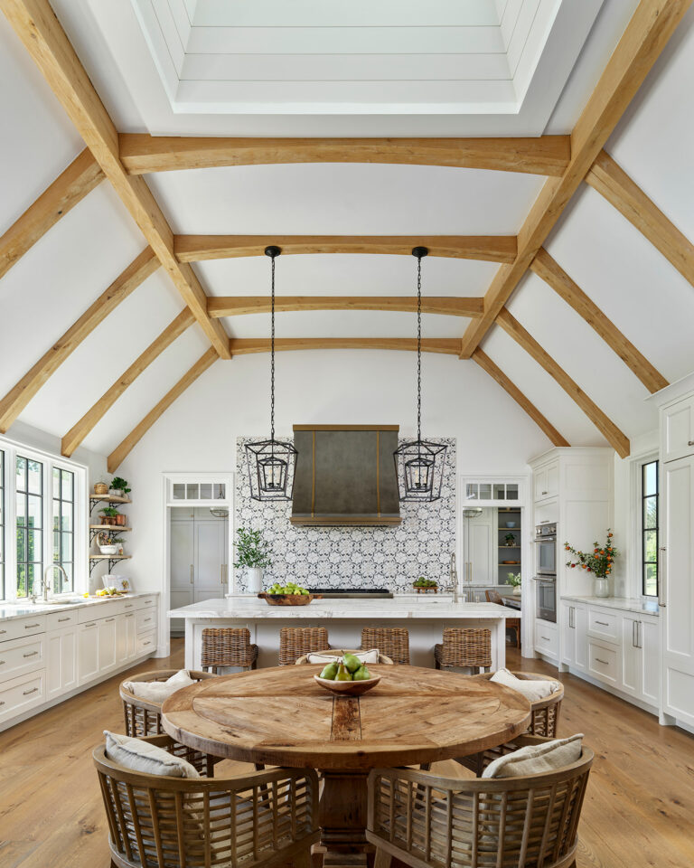 Kitchen and eating area in Chestnut Fields, a contemporary farmhouse with white walls, timber frame vaulted ceiling, white cabinets, island, custom range hood and patterned tile accent wall.