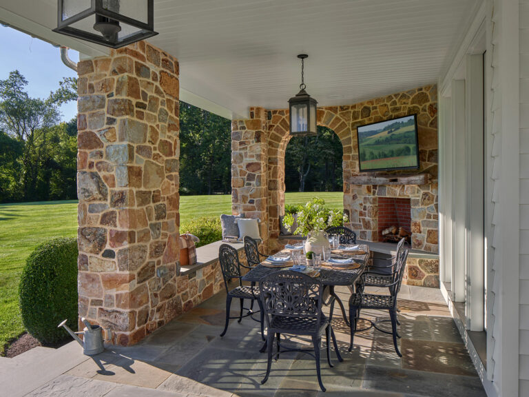 Covered terrace with fieldstone arch, hanging lanterns and outdoor fireplace at Evergreen Farm